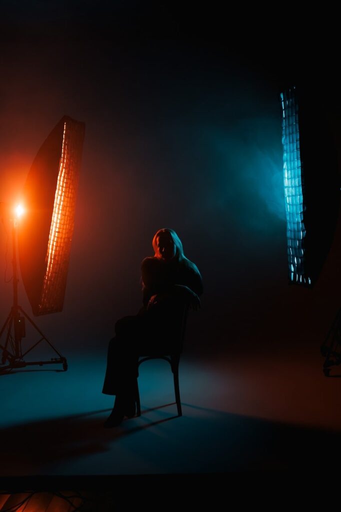 silhouette, stage, lighting, neon light, studio photography, pose, portrait, fashion, model, black, blue, orange, darkness, atmosphere, artistic, performance, woman, creativity, emotional, person, chair