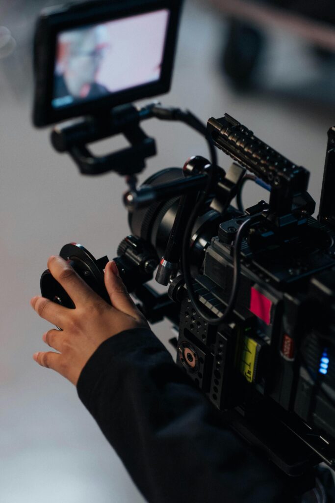 Hands adjusting professional video camera on set, focusing on filming setup.